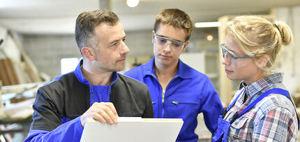 Ausbildung der Ausbilder Ein Ausbilder erklärt zwei jungen Auszubildenden in Arbeitskleidung eine Ausbildungssituation.