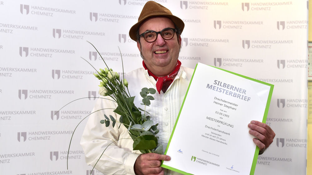 Ein Drechslermeister hält seinen Silbernen Meisterbrief und Blumen in der Hand.